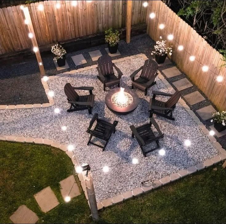 Six dark Adirondack chairs arranged around a glowing circular fire pit on a gravel patio.