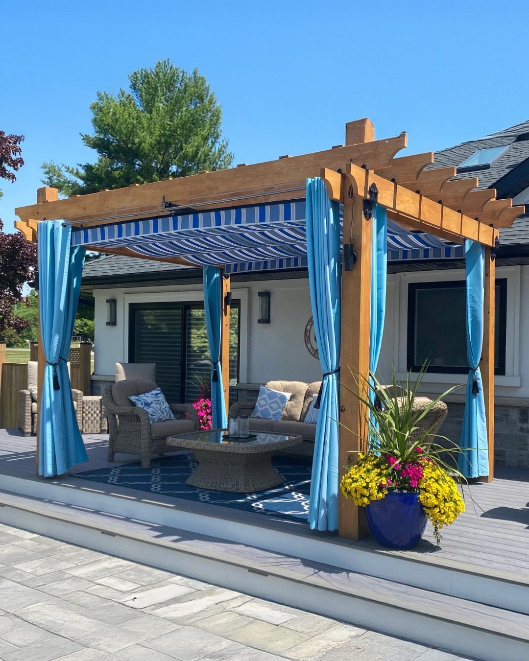 Wooden pergola with blue striped shade canopy and curtains over a patio lounge set.