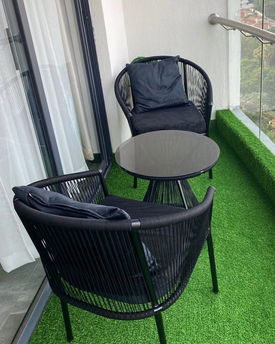 Black woven bistro set with two chairs and a round table on green turf.