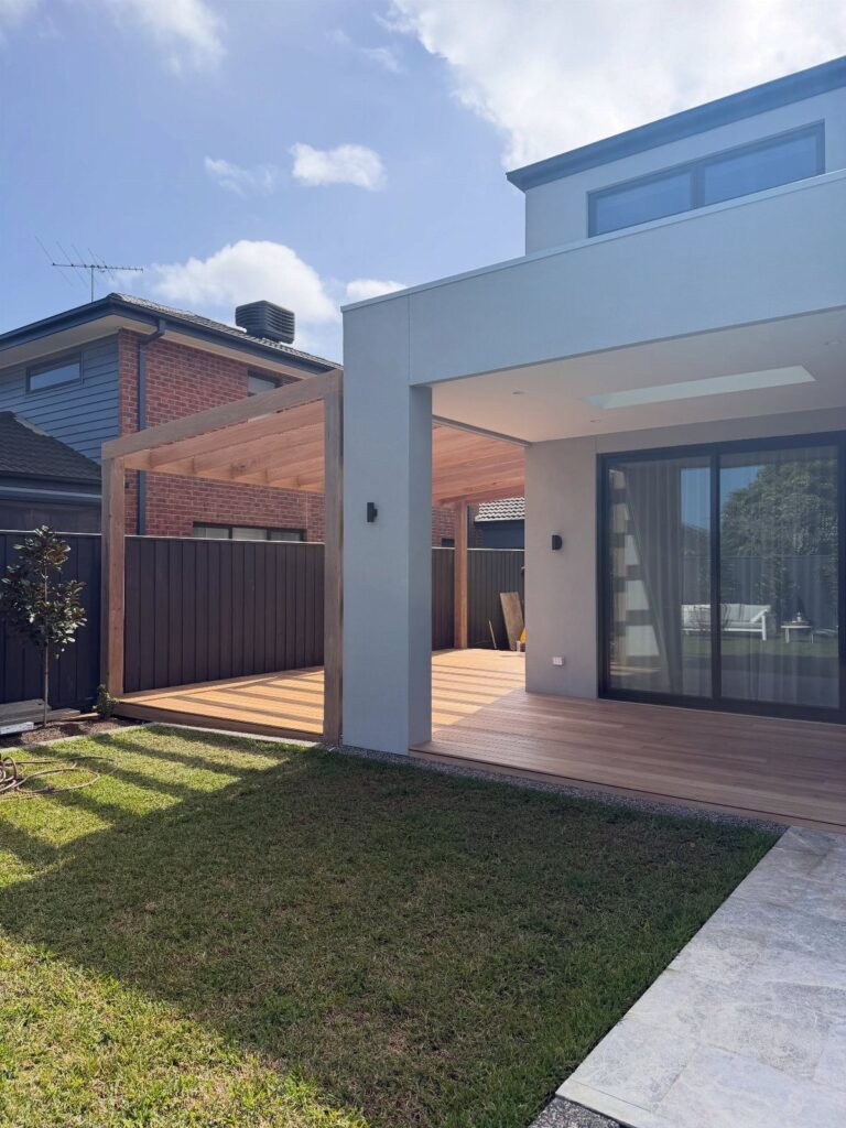 A modern house with an attached wooden deck and a wooden pergola structure over the patio.