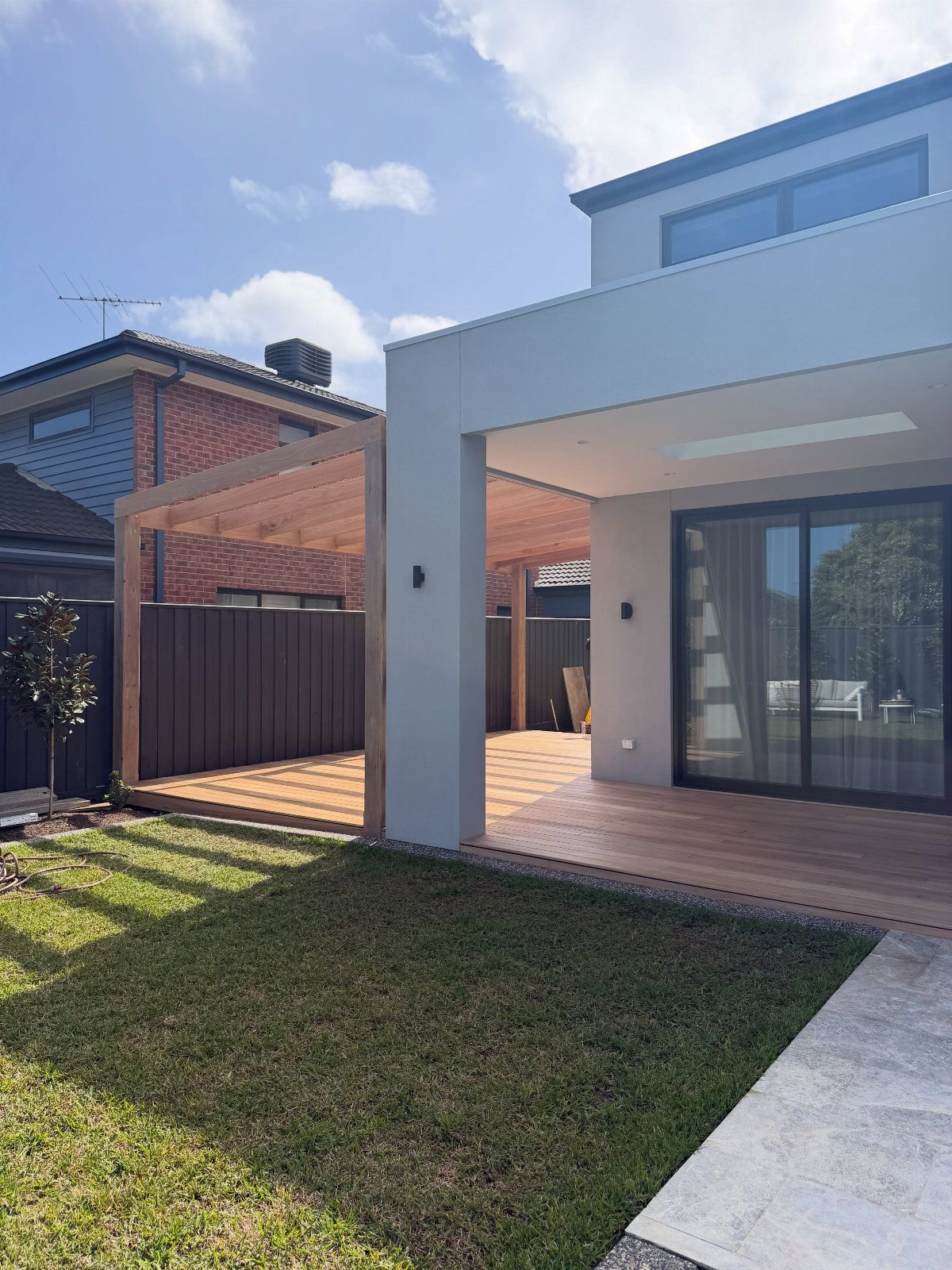 A modern house with an attached wooden deck and a wooden pergola structure over the patio.