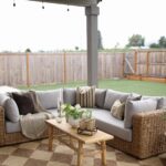 Grey outdoor sectional sofa with cushions and a wicker base on a checkered rug.