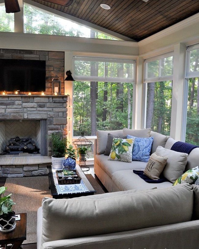 A cozy sunroom featuring a stone fireplace, large windows, and a comfortable sectional sofa.